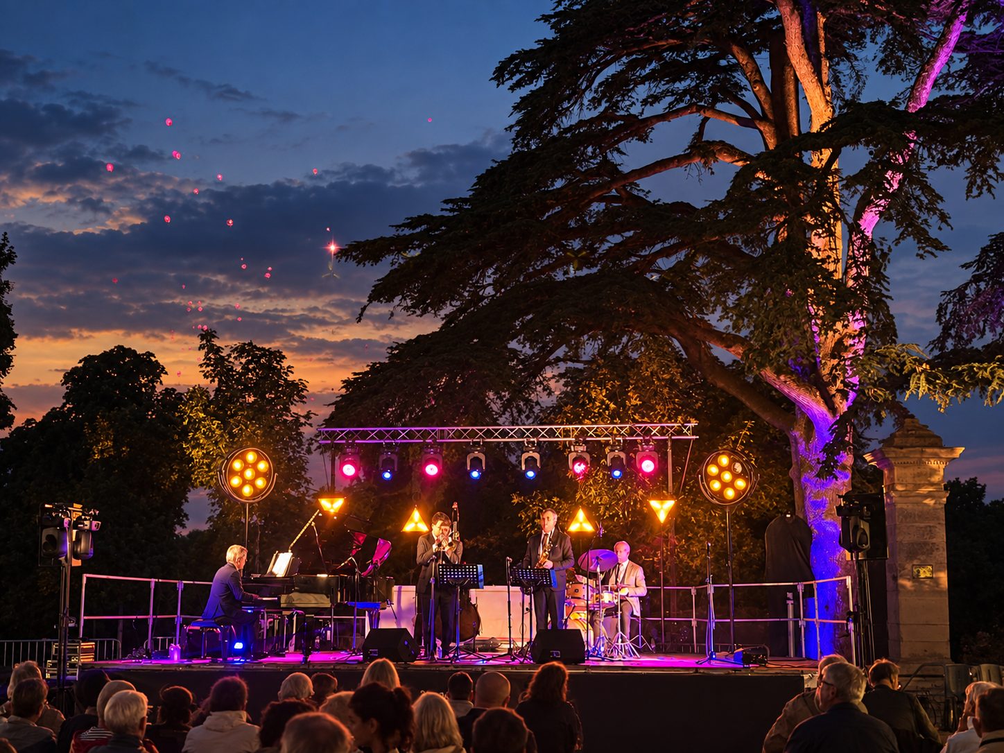 Scène et arbres mis en lumière pendant un concert à la tombée de la nuit