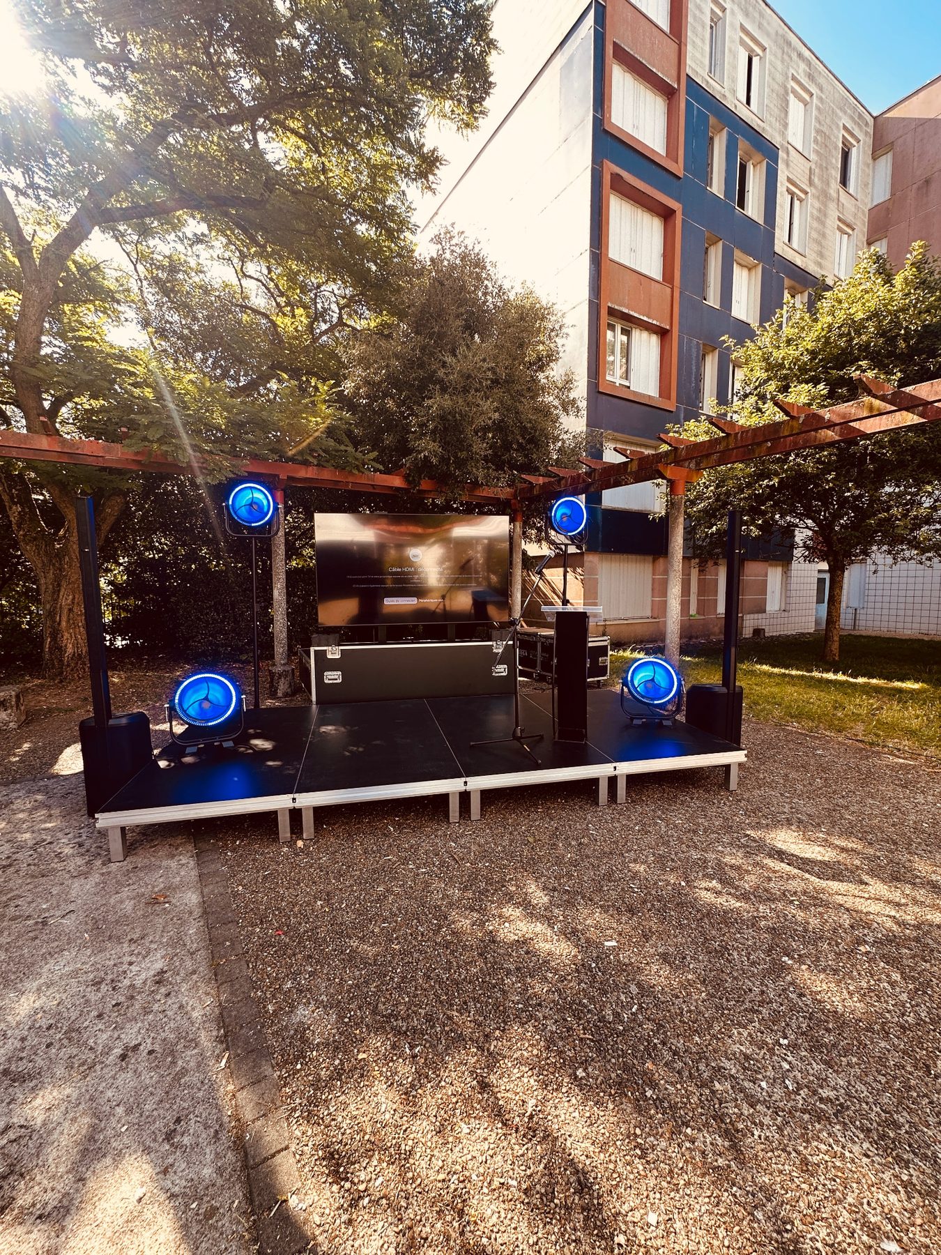 Podium et écran installés dans un jardin avec projecteurs bleus