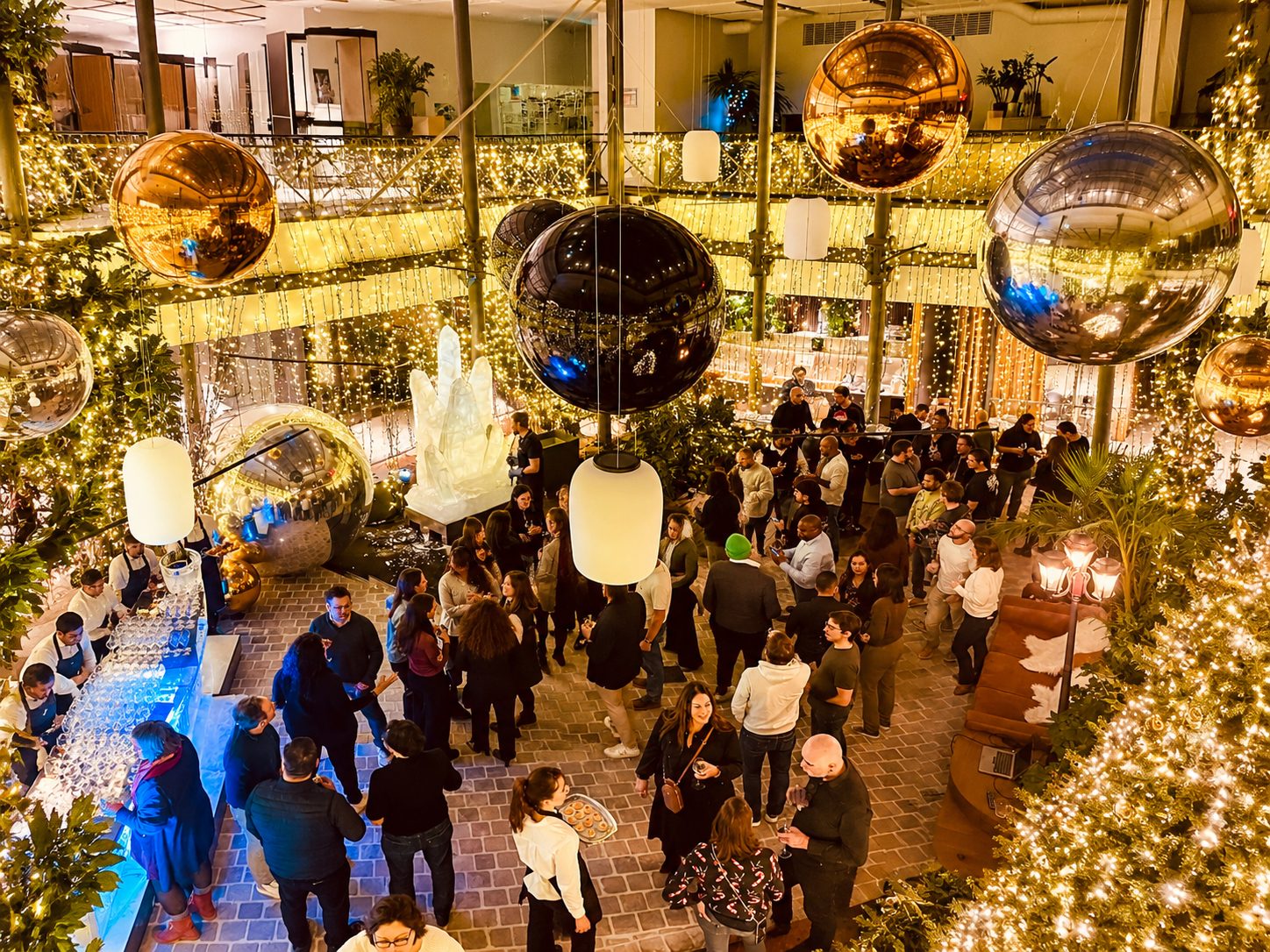 Invités dans un atrium décoré de guirlandes dorées et de grandes sphères miroir