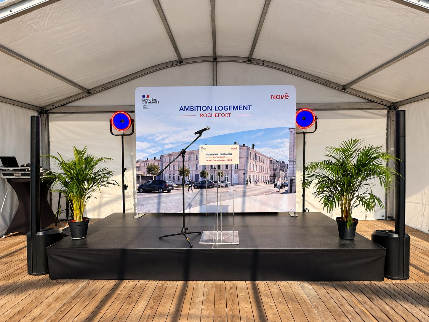 Scène d’inauguration sous une tente avec pupitre, micros, écran et sonorisation