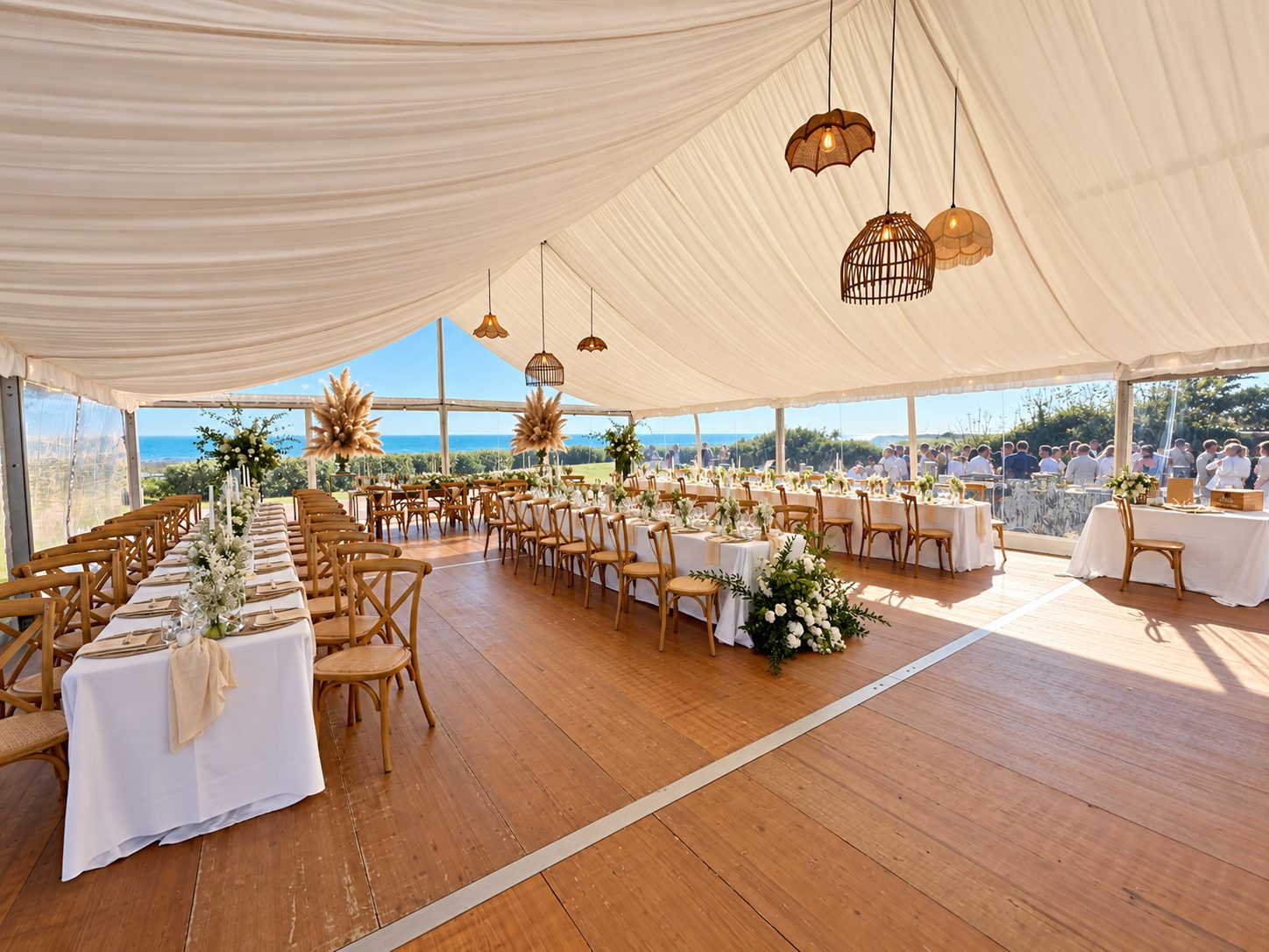 Vue d’ensemble des tables de mariage sous une tente drapée face à la mer