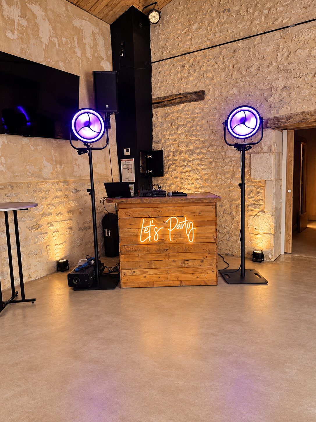 Installation DJ en bois dans une salle en pierre avec projecteurs violets et lumière ambrée
