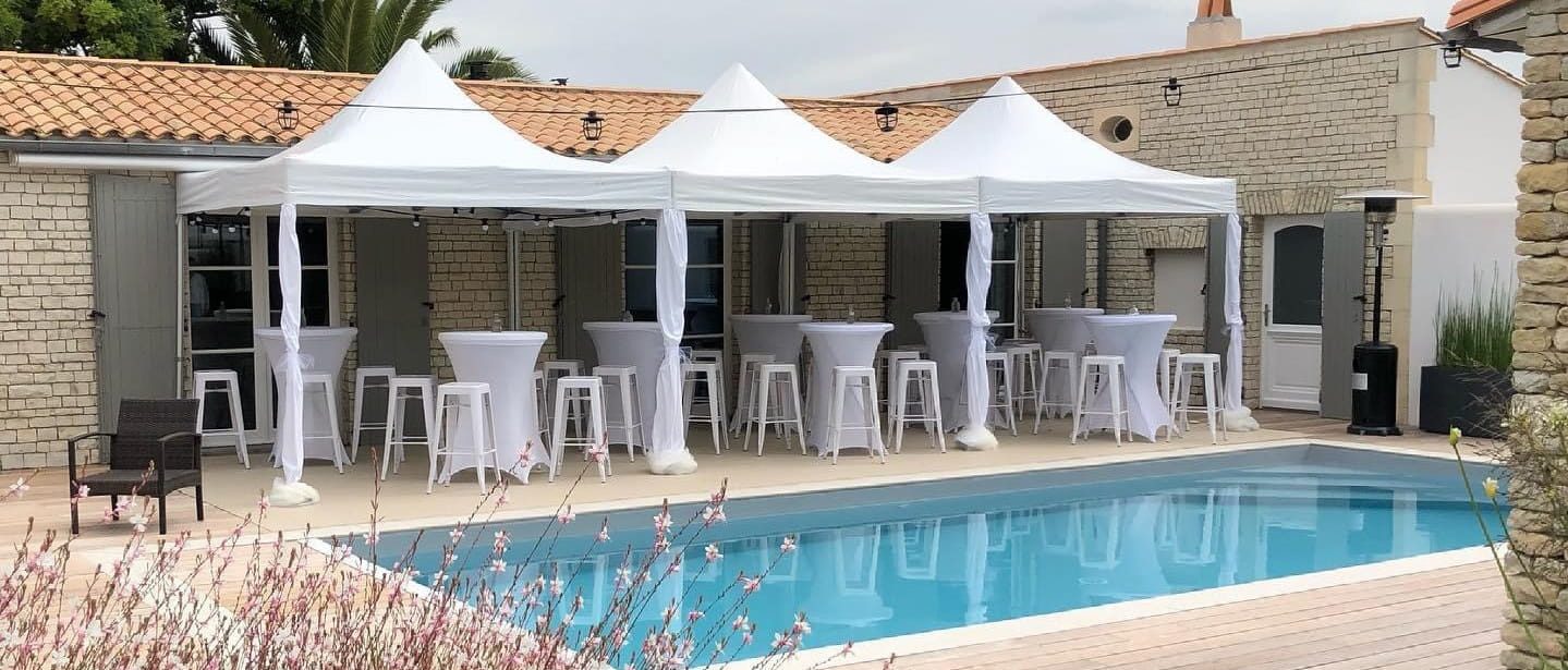Tentes blanches et mange-debout installés pour une réception au bord d’une piscine